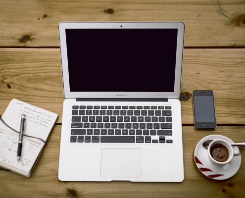 laptop on wooden surface with notebook, pen, iphone, and espresso