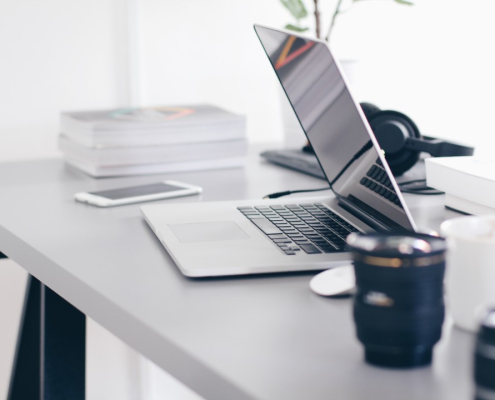 desk with laptop, coffee, phone, books, headphones, and mouse