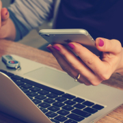 female hands holding iphone while working on laptop