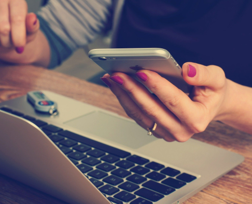 female hands holding iphone while working on laptop