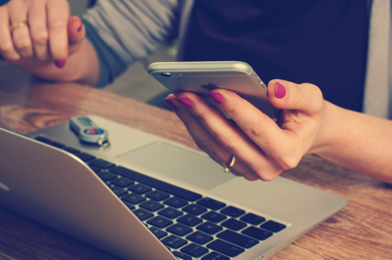 female hands holding iphone while working on laptop