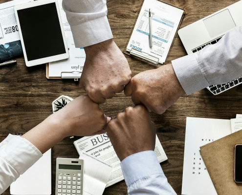 four hands fist bumping over conference room table