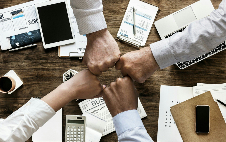 four hands fist bumping over conference room table