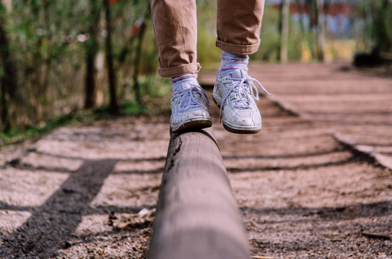 person with white shoes balancing on wooden pole