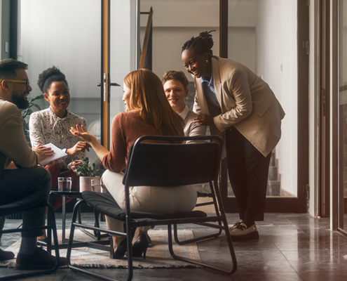 A diverse group of five legal and business professionals meeting informally in an office lounge, reflecting the collaborative, cross-functional relationships in-house counsel build with teams like HR, finance, and operations.