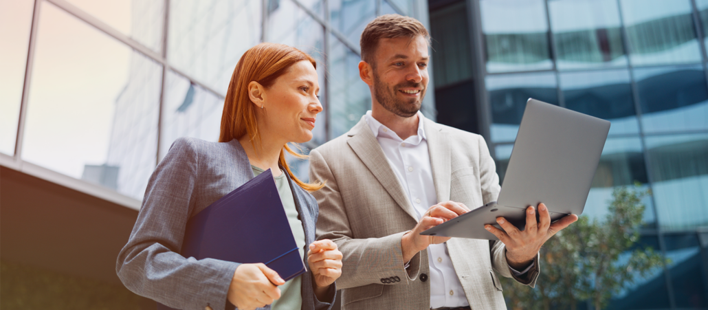 An attorney and a business colleague reviewing information on a laptop together outside a corporate office, representing the kind of stakeholder collaboration and business partnership central to in-house counsel roles.