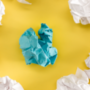 Alt text: Crumpled paper balls on yellow background with one blue paper in the center.