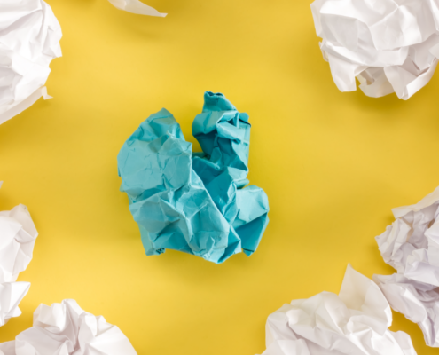 Crumpled paper balls on yellow background with one blue paper in the center.