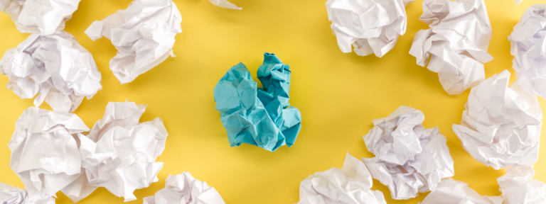 Crumpled paper balls on yellow background with one blue paper in the center.