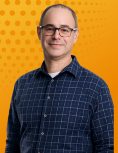 Portrait of a legal executive (Ron Bell) wearing glasses and a navy checkered shirt against an orange background.