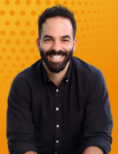 Portrait of a smiling legal leader (Andrew Epstein) with a beard wearing a black button-down shirt against an orange background.