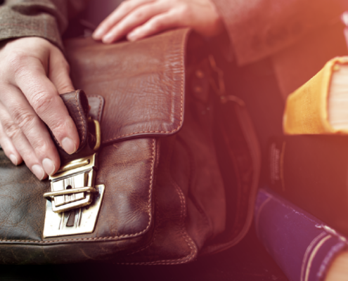 Person holding a leather briefcase beside a stack of books.